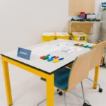 Training Station 1 prepared for Lean Manufacturing Training, with colorful components, worksheets, and process materials on a yellow-framed table.