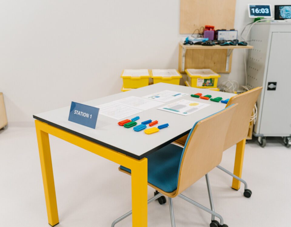 Training Station 1 prepared for Lean Manufacturing Training, with colorful components, worksheets, and process materials on a yellow-framed table.