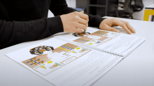 Participant reading a guidebook with illustrated instructions during a lean manufacturing games simulation. 