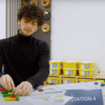 Participant engaged in a lean gaming simulation at Station 4 using colorful plastic blocks.