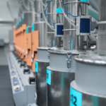 Row of stainless-steel dosing hoppers and orange control modules in a spotless, clearly-marked production cell.