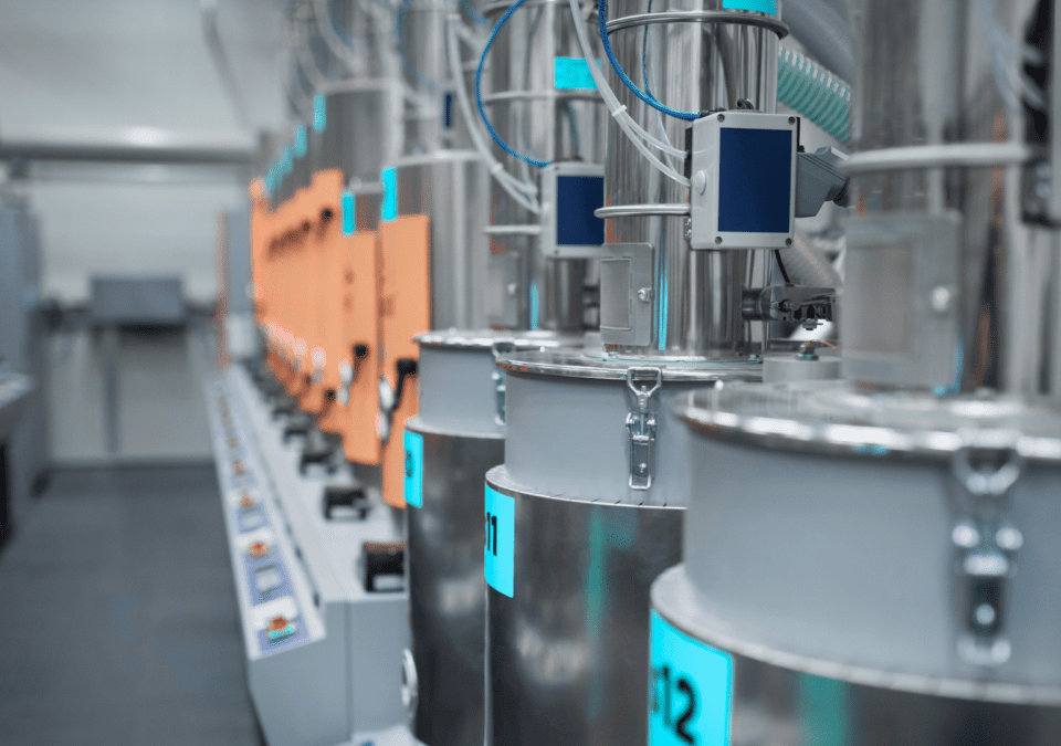 Row of stainless-steel dosing hoppers and orange control modules in a spotless, clearly-marked production cell.