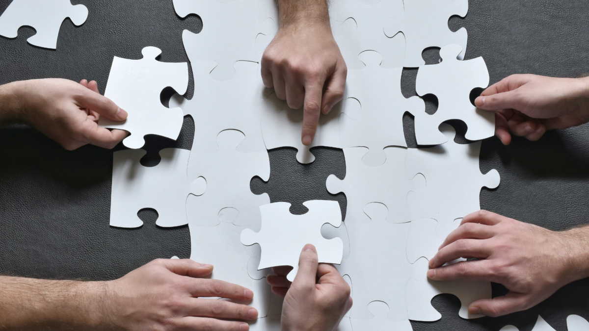 Hands putting together puzzle pieces during a teamwork trainings activity.