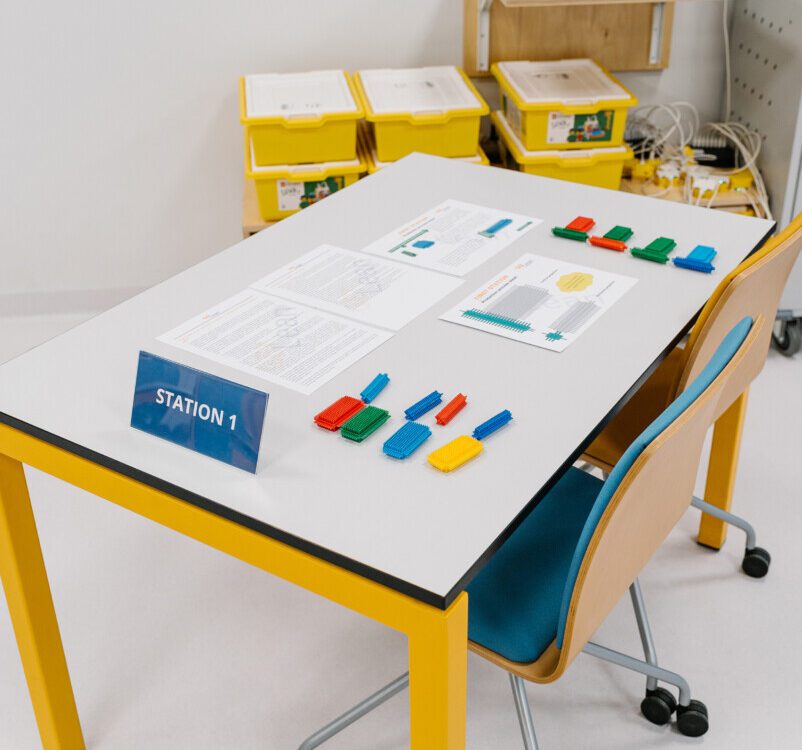 Station-1 setup for a Lean Manufacturing Simulation Game, displaying instruction sheets and colour-coded brick parts arranged for assembly.