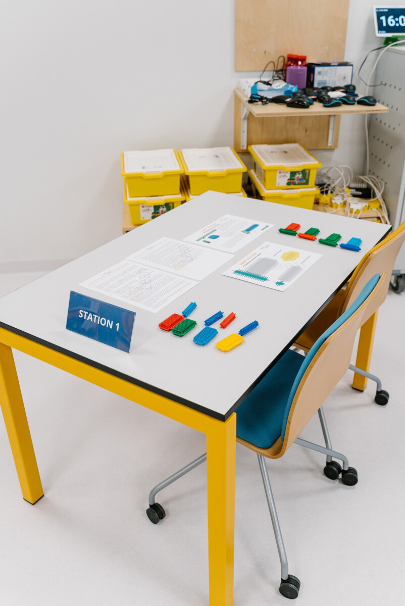 Station-1 setup for a Lean Manufacturing Simulation Game, displaying instruction sheets and colour-coded brick parts arranged for assembly.	