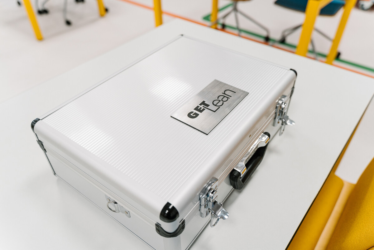 Aluminium briefcase labelled “GET Lean” sitting on a classroom table—portable kit for Lean Simulation training.