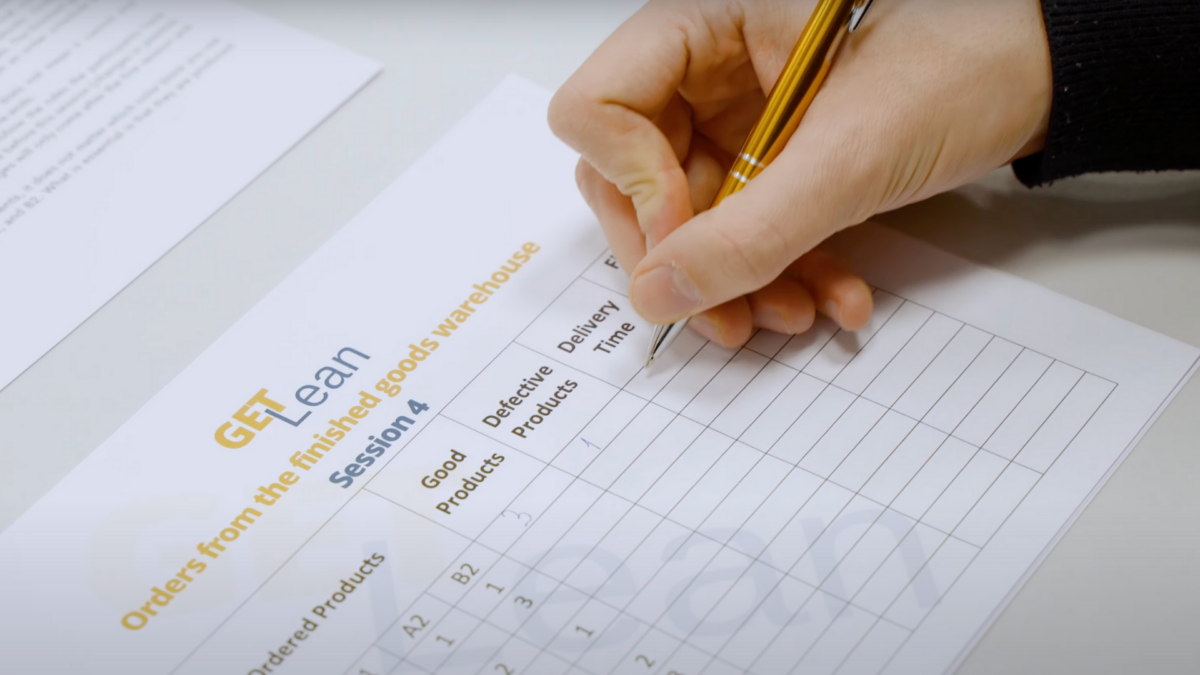 Hand filling out a performance tracking sheet during a Training Lean Manufacturing session using the GET LEAN simulation.