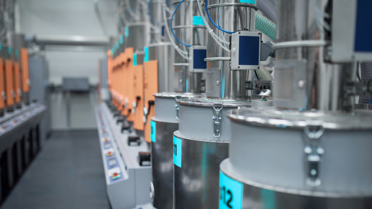 Row of stainless-steel dosing hoppers and orange control modules in a spotless, clearly-marked production cell. 
