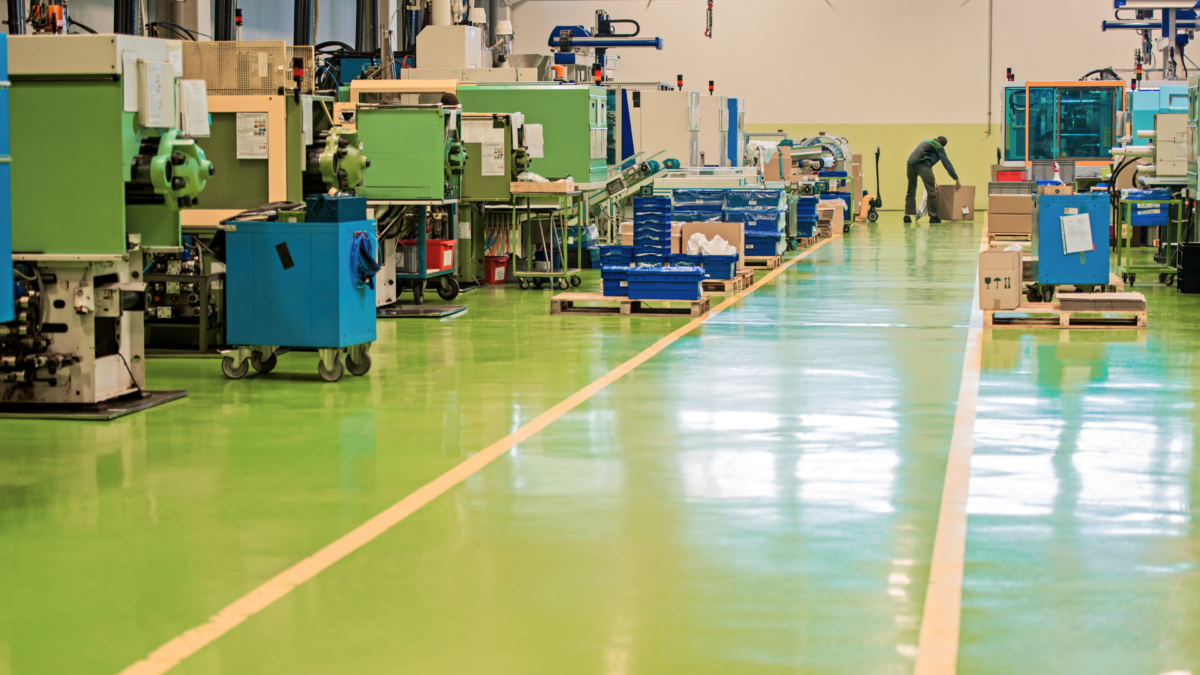 Lean factory floor with bright-green epoxy floor, clear yellow flow lines, evenly spaced CNC and injection-moulding machines, and mobile blue tool carts.